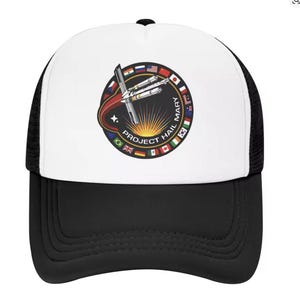 Puede incluir: Gorra de camionero en blanco y negro con un parche circular con el texto "PROJECT HAIL MARY" y una imagen de un cohete. El parche está rodeado de banderas de diferentes países. La gorra tiene un panel frontal blanco y una parte trasera de malla negra.