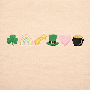 May include: Embroidered St. Patrick's Day themed patches. Includes a green shamrock, rainbow, shooting star, green leprechaun hat, pink heart, and a black pot of gold. The patches are on a light beige background.
