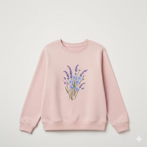 May include: A light pink sweatshirt featuring a floral design. The design is a bouquet of lavender and blue flowers. The sweatshirt has a crew neck and long sleeves.