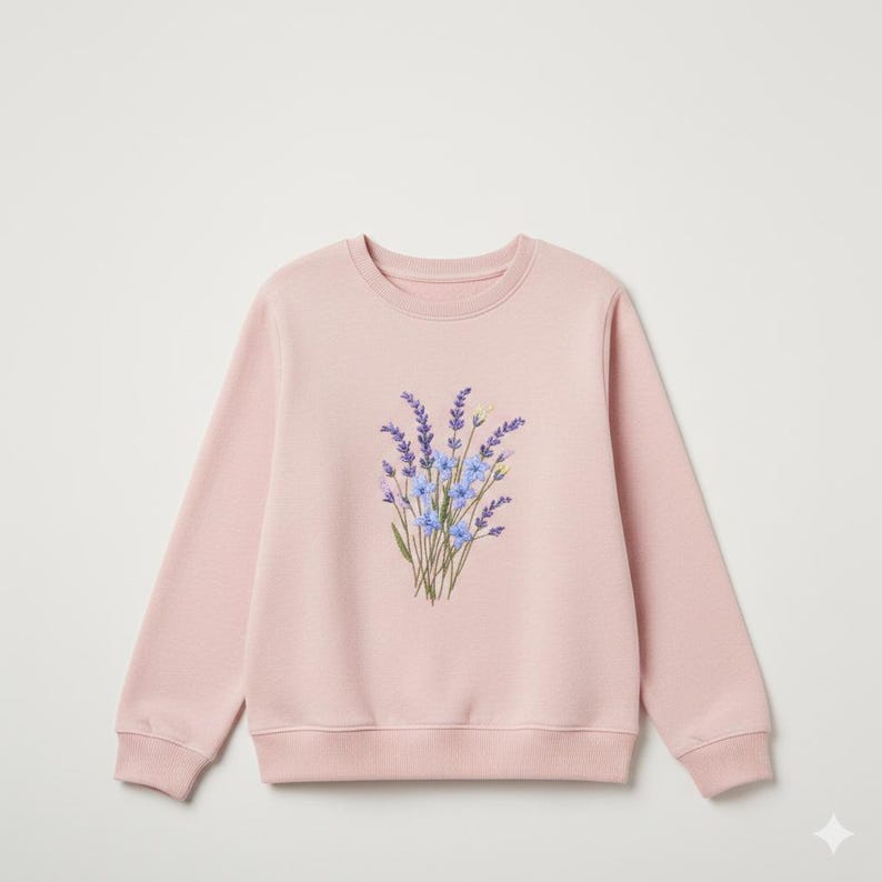 May include: A light pink sweatshirt featuring a floral design. The design is a bouquet of lavender and blue flowers. The sweatshirt has a crew neck and long sleeves.