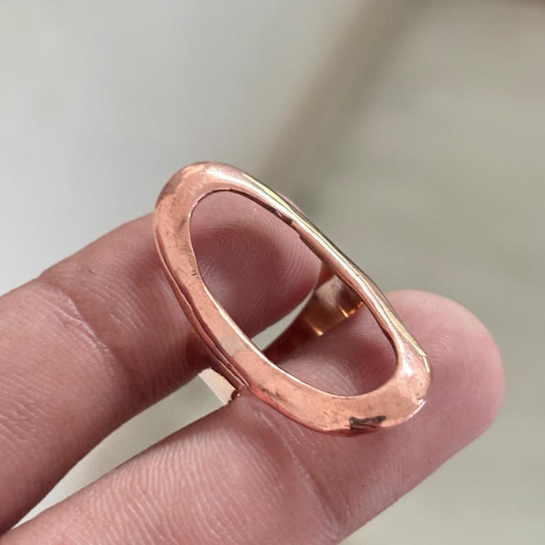 Pode incluir: Um anel em tom de ouro rosa com uma estrutura aberta grande em formato oval alongado. A superf&iacute;cie met&aacute;lica apresenta um acabamento levemente martelado e texturizado com um brilho quente, formando um aro cont&iacute;nuo ao redor do dedo.