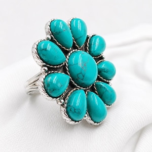 May include: A silver ring featuring a large, round, central turquoise stone surrounded by eight smaller, pear-shaped turquoise stones. Each stone is set in a twisted silver frame, creating a floral arrangement with a polished silver band.