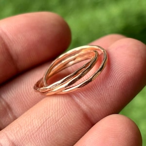 Könnte beinhalten: Ein Satz von drei ineinandergreifenden goldenen Ringen mit gehämmerten Texturen. Die Ringe haben eine warme Goldfarbe und scheinen handgefertigt zu sein. Die Ringe werden vor einem verschwommenen grünen Hintergrund gezeigt.