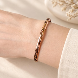 May include: A tri-colour metal bangle bracelet featuring a twisted, rope-like design. The bracelet is composed of alternating polished segments in yellow gold, rose gold, and silver tones, creating a continuous spiral pattern around the wrist.