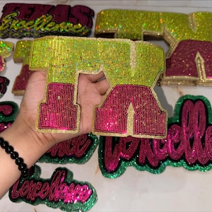 May include: A collection of sequined patches in various shapes and sizes. The patches feature the word "Texas" and "Excellence" in a mix of colors, including green, pink, and gold. The patches are likely for clothing or accessories.