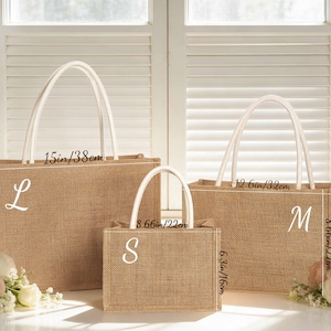 Puede incluir: Tres bolsas de mano de yute de diferentes tama&ntilde;os con asas blancas. La bolsa m&aacute;s grande mide 38 cm de ancho y 27 cm de alto, con una "L". La bolsa mediana mide 32 cm de ancho y 22 cm de alto, con una "M". La bolsa m&aacute;s peque&ntilde;a mide 22 cm de ancho y 16 cm de alto, con una "S".