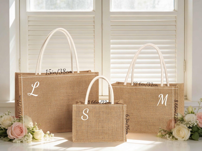 Puede incluir: Tres bolsas de mano de yute de diferentes tama&ntilde;os con asas blancas. La bolsa m&aacute;s grande mide 38 cm de ancho y 27 cm de alto, con una "L". La bolsa mediana mide 32 cm de ancho y 22 cm de alto, con una "M". La bolsa m&aacute;s peque&ntilde;a mide 22 cm de ancho y 16 cm de alto, con una "S".