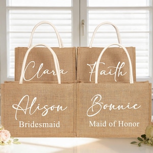 May include: Four burlap tote bags with white handles and personalized names in elegant script. The bags are labeled "Clara", "Faith", "Alison - Bridesmaid", and "Bonnie - Maid of Honor". The bags are arranged in front of a window.