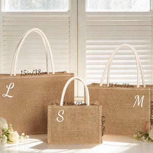 May include: Three burlap tote bags of varying sizes with white handles. The largest bag is 15 inches wide and 10.6 inches tall, labeled with an "L". The medium bag is 12.6 inches wide and 8.66 inches tall, labeled with an "M". The smallest bag is 8.66 inches wide and 6.3 inches tall, labeled with an "S".