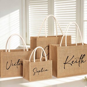 May include: A collection of burlap tote bags with white handles. Each bag has a name printed in black script: Victor, Sophia, Keith. The bags are in various sizes and are likely for a special event or gift.