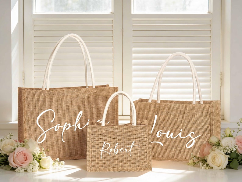 May include: Three burlap tote bags with white handles and custom names in a cursive font. The largest bag says "Sophia", the medium bag says "Louis", and the smallest bag says "Robert". The bags are sitting in front of a window with flowers.