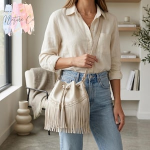 Può includere: Una borsa a secchiello color crema con frange e chiusura con coulisse. La borsa ha una lunga tracolla ed è realizzata in un materiale morbido e strutturato. La borsa fa parte della collezione Nature Co.