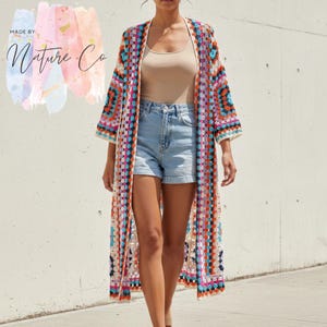 Puede incluir: Un cárdigan largo de crochet con frente abierto en un diseño de patchwork colorido. El cárdigan presenta una mezcla de colores brillantes que incluyen naranja, rosa, azul y blanco. El texto "MADE BY: Nature Co" es visible en la esquina superior izquierda.