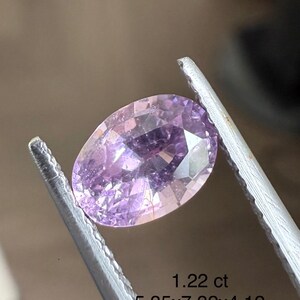May include: A faceted, oval-shaped, light purple gemstone is held by a pair of silver tweezers. The gem is 5.35 x 7.32 x 4.12 mm and weighs 1.22 ct. The gem has a brilliant cut and is a light lavender color.
