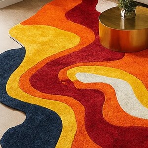 May include: A colorful, abstract area rug with a wavy design. The rug features bands of navy blue, white, yellow, orange, and red. The rug is on a hardwood floor, with a gold side table and a beige sofa in the background.