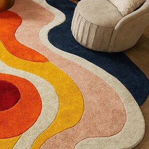 May include: A colorful, abstract area rug with a wavy design. The rug features a combination of colors, including orange, yellow, pink, cream, and navy blue. The rug is placed on a wooden floor, with beige furniture in the background.