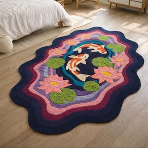 May include: A colorful, wavy-edged rug featuring a koi pond design. The rug has a dark blue border, with layers of pink, purple, and blue. The center depicts two koi fish, pink lotus flowers, and green lily pads.