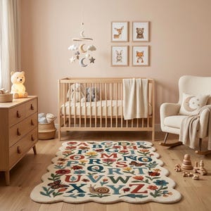 May include: A nursery scene with a wooden crib, dresser, and rocking chair. A cream-colored rug with an alphabet design and floral accents sits on the floor. The room is decorated with framed animal prints and a mobile with moon and star shapes.