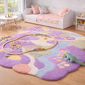 May include: A whimsical, cloud-shaped rug in shades of purple, pink, and green, featuring a wooden train track and a plush dinosaur toy. The rug is placed on a hardwood floor in a child's room, with a white daybed and small table visible in the background.
