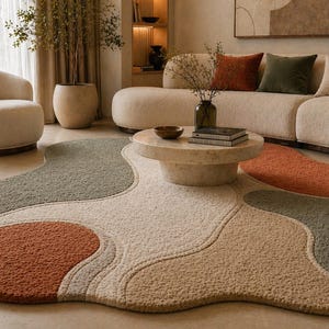 May include: A modern living room featuring a cream-colored sofa with decorative pillows, a round marble coffee table, and a unique area rug with abstract shapes in shades of beige, rust, and green. A matching armchair is also present.