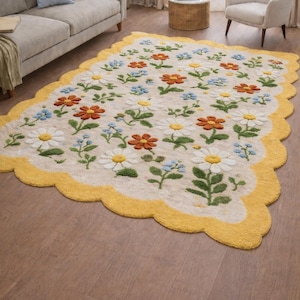 May include: A floral area rug with a cream-colored background and a yellow scalloped border. The rug features a pattern of daisies, orange flowers, and blue flowers with green leaves. The rug is placed on a hardwood floor.