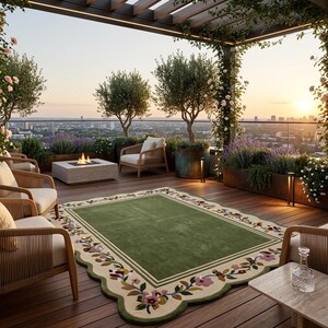 May include: A rectangular area rug featuring a solid green centre, a cream-coloured border, and a scalloped edge decorated with a colourful floral pattern of pink, red, and yellow flowers with green leaves, placed on a wooden deck.