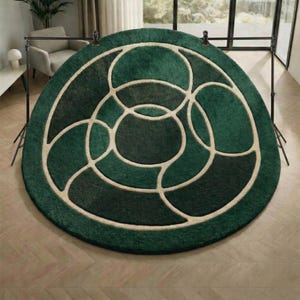 May include: A round, green rug with a geometric design. The rug features a pattern of interlocking circles in varying shades of green, outlined with a cream-colored border. The rug is placed on a wooden floor.