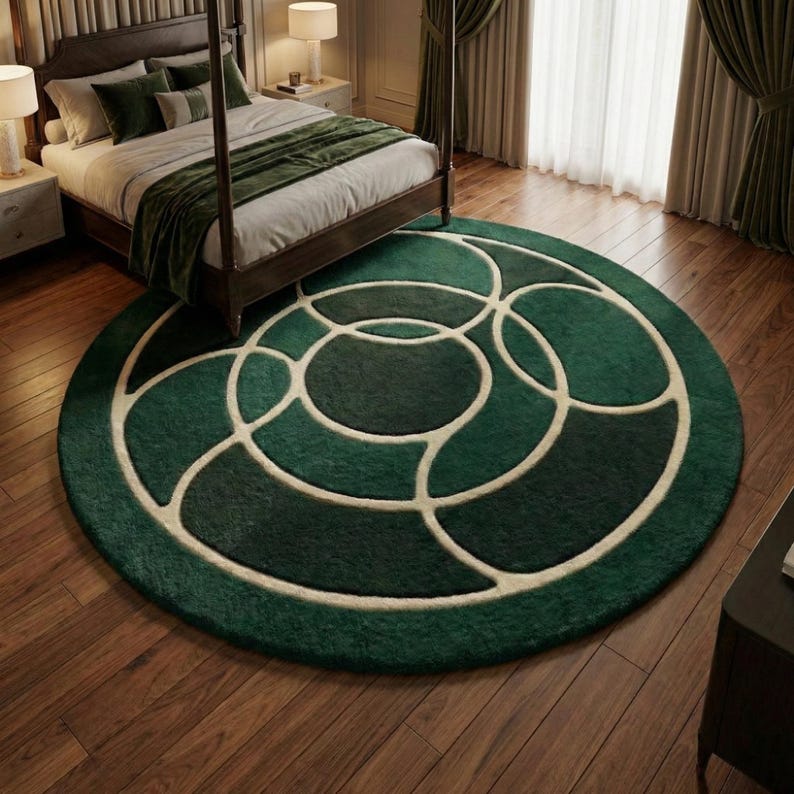 May include: A round, emerald green rug with a geometric design of overlapping circles in varying shades of green and cream. The rug is placed on a hardwood floor in a bedroom setting, with a bed visible in the background.