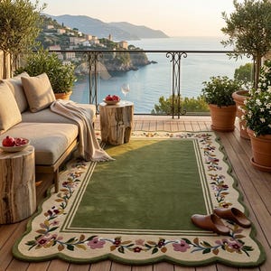May include: A rectangular area rug featuring a solid olive green centre, a cream-coloured border, and a scalloped edge decorated with embroidered floral vines in shades of pink, yellow, and brown, placed on a wooden deck with brown leather slippers.