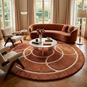 May include: A living room scene featuring a rust-colored curved sofa, two armchairs, and a round rug with an abstract design in shades of orange and cream. A marble coffee table and two floor lamps complete the decor.