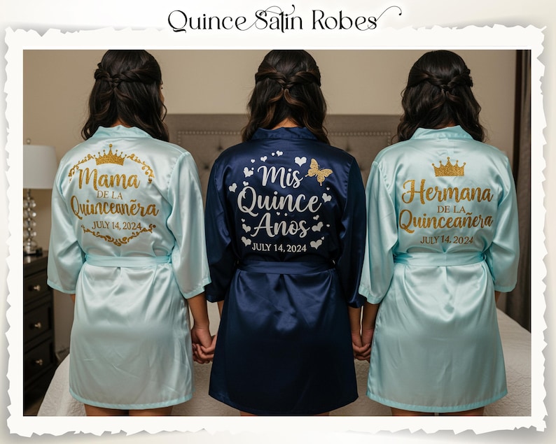 Peut inclure: Trois peignoirs en satin, deux bleu clair et un bleu marine, avec des textes dor&eacute;s et des motifs de couronnes. Les peignoirs sont pour une c&eacute;l&eacute;bration de quincea&ntilde;era, avec les textes "Mama", "Mis Quince A&ntilde;os", et "Hermana", avec la date du 14 juillet 2024.