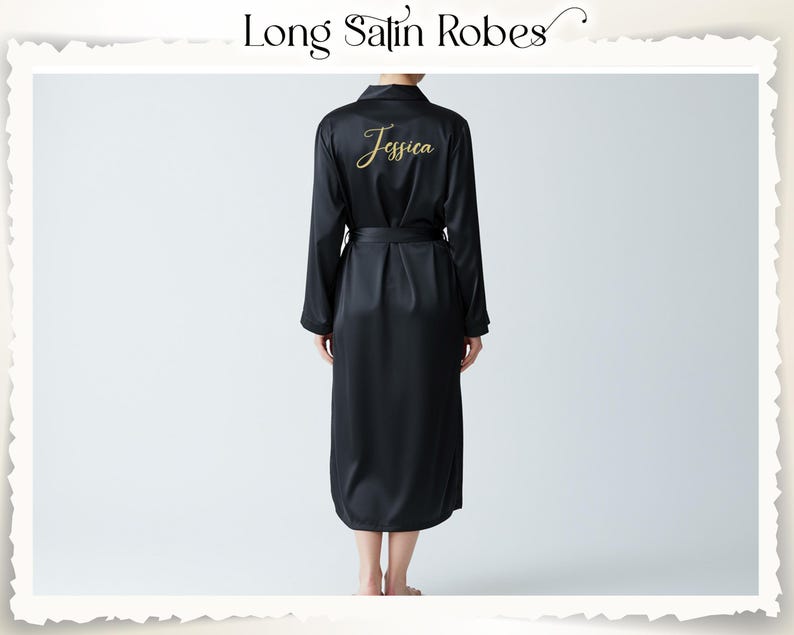 A long black satin robe with a matching belt. The word "Jessica" is embroidered in gold script on the back. The robe has long sleeves and a collared neckline. The text "Long Satin Robes" is at the top.