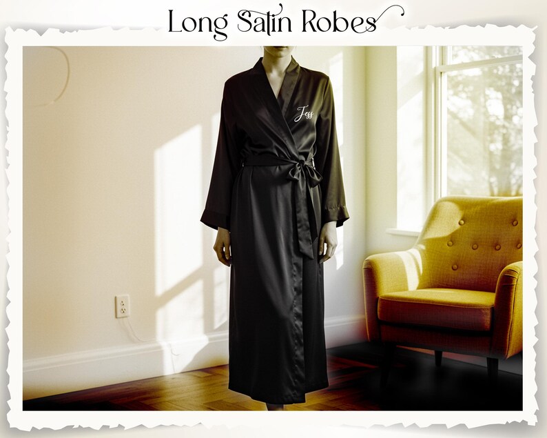 May include: A long black satin robe with a tie waist and long sleeves. The robe has the word "Jess" embroidered on the chest. The image also includes the text "Long Satin Robes". A yellow armchair is in the background.