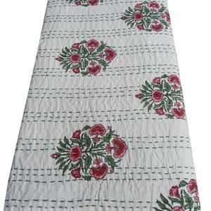 May include: White quilt with a floral pattern. The quilt features clusters of pink flowers with green leaves, evenly spaced across the surface. The design is stitched with green thread, creating a textured appearance. The quilt is folded.
