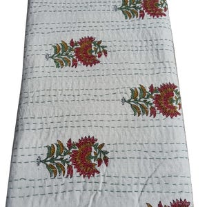May include: White quilted fabric with a floral pattern in red, yellow, and green. The flowers are arranged in a repeating pattern across the fabric. The stitching is visible in a grid pattern.