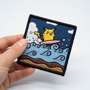 Puede incluir: Parche bordado con Pikachu surfeando en una tabla rosa. El diseño incluye olas azules del océano, nubes blancas y un fondo azul oscuro. El parche tiene un borde negro.