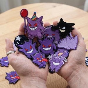 May include: A collection of embroidered patches featuring various purple and black cartoon characters with red eyes and white smiles. One character holds a red balloon. The patches are in various shapes and sizes, with detailed stitching.