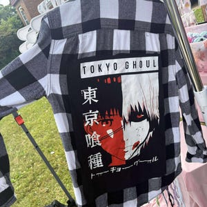 Könnte beinhalten: Schwarz-weiß kariertes Flanellhemd mit Grafik auf dem Rücken. Die Grafik zeigt den Text "TOKYO GHOUL" und eine rot-weiße Illustration einer Figur.