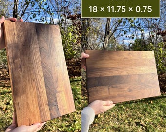 May include: A walnut cutting board, measuring 18 x 11.75 x 0.75 inches, is held up in front of a natural background. The wood grain is visible, with variations in color from light to dark brown. The text "walnut" and the dimensions are displayed.