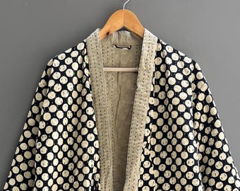 May include: A long-sleeved robe featuring a black fabric base with a repeating pattern of white circles. The garment includes a solid beige collar and front trim, two large front pockets, and a matching tie belt. The text Chandrahandicraft is visible.
