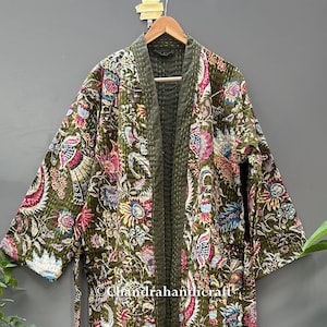 May include: Olive green quilted robe with a floral pattern in pink, blue, and white. The robe has a dark green trim and a matching belt. The text "Chandrahancraft" is visible on the robe.