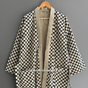 May include: A black and white polka dot patterned robe. The robe has a light beige interior and trim. It features long sleeves and a tie belt. The robe is made of a soft, comfortable material. The robe is a stylish garment.