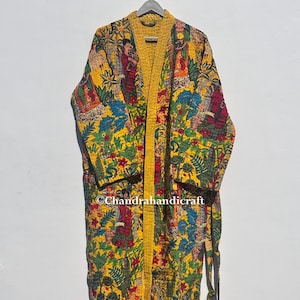 Könnte beinhalten: Ein langer, gelber Bademantel mit einem lebendigen, gemusterten Design. Der Bademantel hat einen farbenfrohen Druck mit Figuren, Pflanzen und floralen Elementen. Der Text "©Chandrahandicraft" ist sichtbar. Der Bademantel hat eine gelbe Einfassung und einen passenden Bindegürtel.
