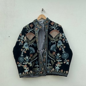 May include: Black embroidered jacket with floral designs in shades of peach, blue, and green. The jacket features a mandarin collar and a striped lining. The jacket is hanging on a wooden hanger.