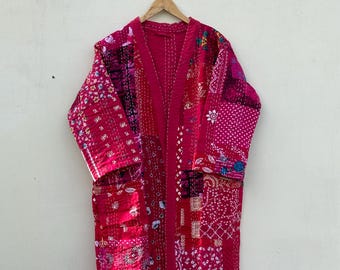 May include: A long, patchwork robe in shades of pink and red, hanging on a wooden hanger. The robe features a variety of patterned fabric squares, stitched together with visible seams. The robe has long sleeves and a relaxed fit.