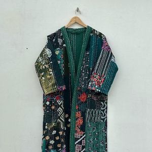 Könnte beinhalten: Langer Patchwork-Robe in Grüntönen mit floralen und geometrischen Mustern. Die Robe besteht aus verschiedenen Stoffstücken, die zusammengenäht sind, mit einem einfarbigen grünen Futter und Besatz. Sie hängt an einem Holzbügel.