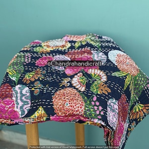 May include: A dark blue floral quilt with a vibrant pattern of pink, orange, yellow, and green flowers. The quilt is hand-stitched with white thread and is draped over a small wooden stool. The text "Chandrahandicraft" is visible.