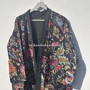 May include: A black quilted kimono-style jacket with a vibrant floral pattern in shades of red, blue, yellow, and pink. The jacket is hanging on a wooden hanger against a white background. The text "Chandrahandicraft" is visible.