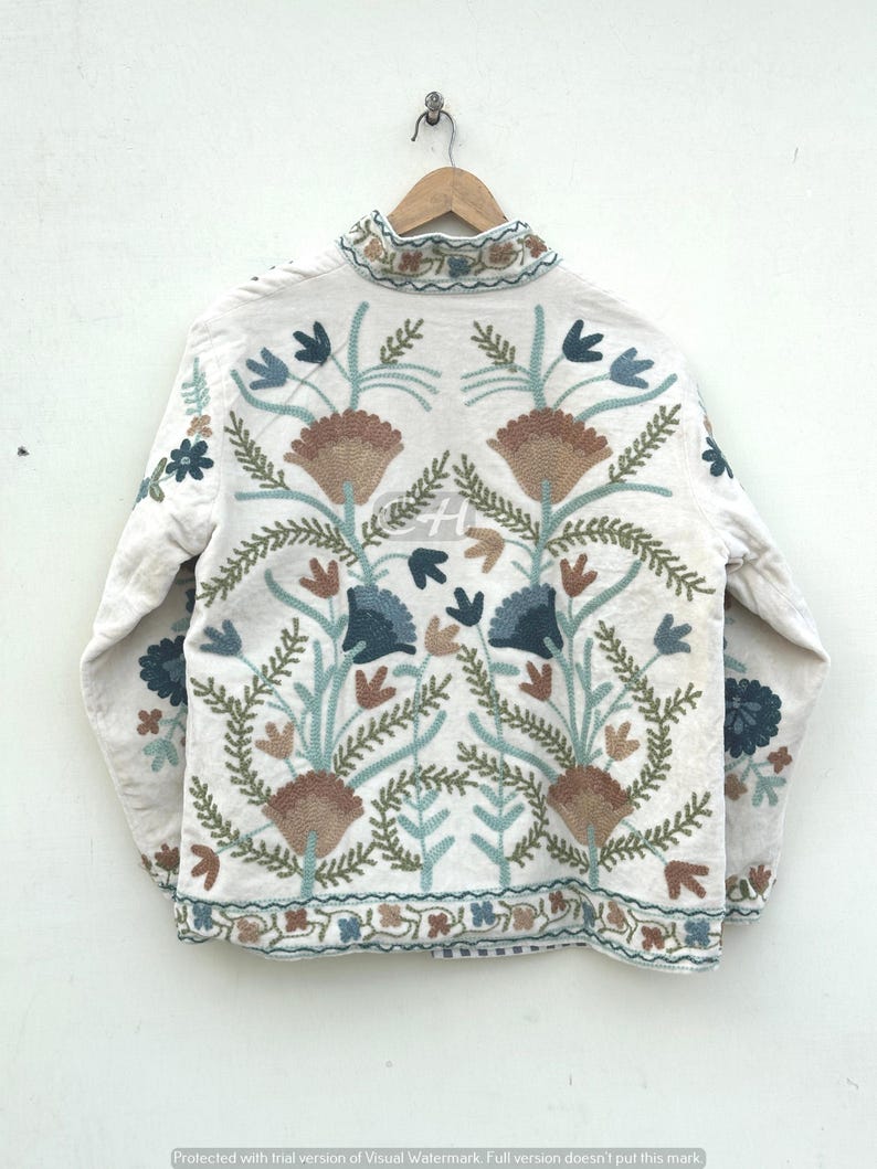 以下が含まれることがあります： クリーム色のジャケット。茶色、青、緑色の複雑な花の刺繍が施されています。ジャケットはハイカラーで、裾と袖口に詳細な刺繍が施されています。デザインには、様式化された花と葉が含まれています。