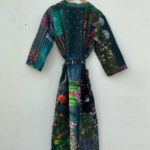 May include: A patchwork robe in shades of green, purple, and red, hanging on a wooden hanger. The robe features a variety of fabric patterns and textures, with a matching belt. The robe is approximately 55 inches long.